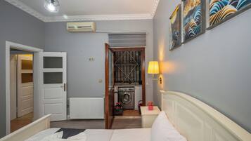 Habitación de hotel con cama, lavadora, radiador y puerta que da a otra estancia.