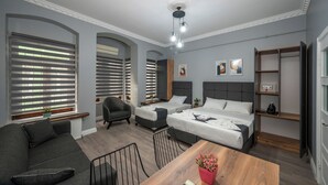Una habitación de hotel moderna con dos camas, un sofá, una mesa de comedor y un ventilador de techo.