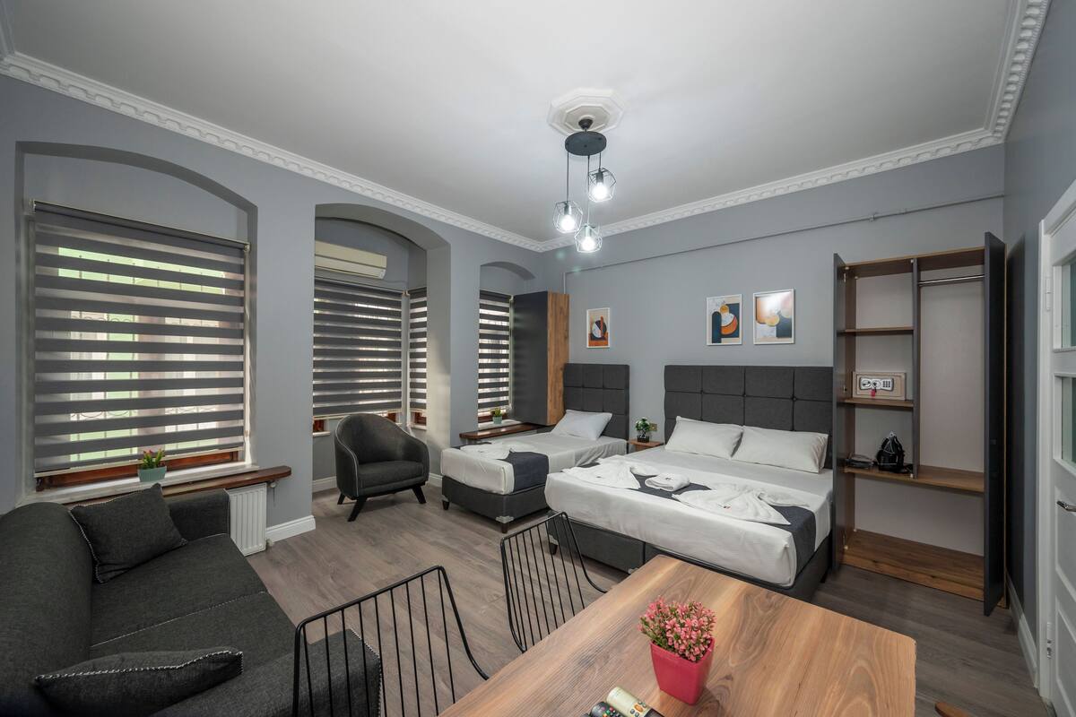 A modern hotel room with two beds, a sofa, a dining table, and a ceiling fan.