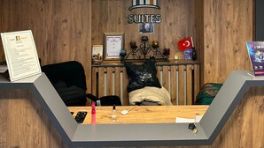 Una recepción con fondo de madera, un letrero que dice 'TAXIM TREND SUITES' y una lámpara circular moderna colgando arriba.