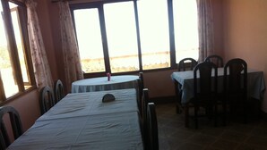 A dining area with a long table and chairs, large windows, and a view of the outdoors. - Mountain Resort (Baluwapati Deupur)