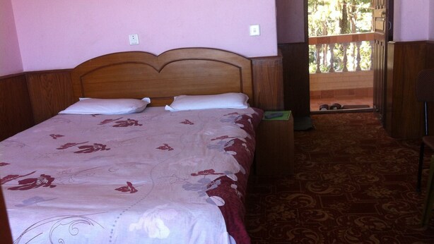 A single bed with a floral bedspread, a wooden headboard, and a nightstand with a lamp. - Mountain Resort (Baluwapati Deupur)