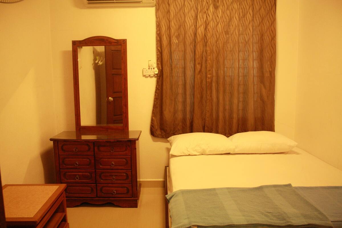 A bedroom with a wooden dresser, a bed with white bedding, and a brown curtain.
