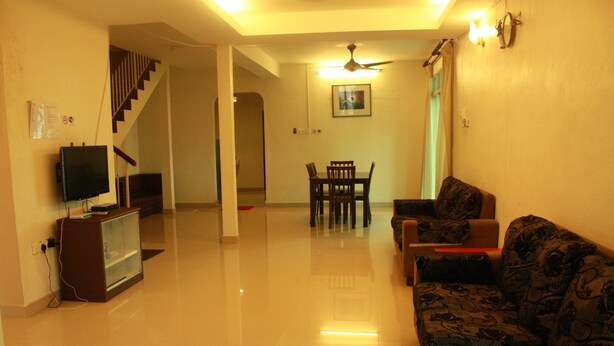 A living room with a sofa, a television, a dining table with chairs, and a staircase leading to another level. - 02 First Island (George Town)