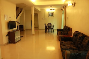 A living room with a sofa, a television, a dining table with chairs, and a staircase leading to another level.