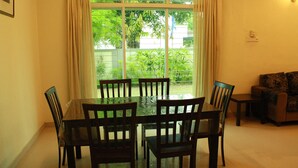 A dining area with a glass table and chairs, a sofa, and a view of greenery outside. - 02 First Island (George Town)