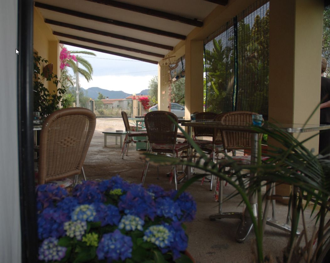 Un espace extérieur aménagé en terrasse, avec des meubles en osier, une table et des chaises. On y trouve des plantes en pot et, au loin, une vue sur les montagnes.
