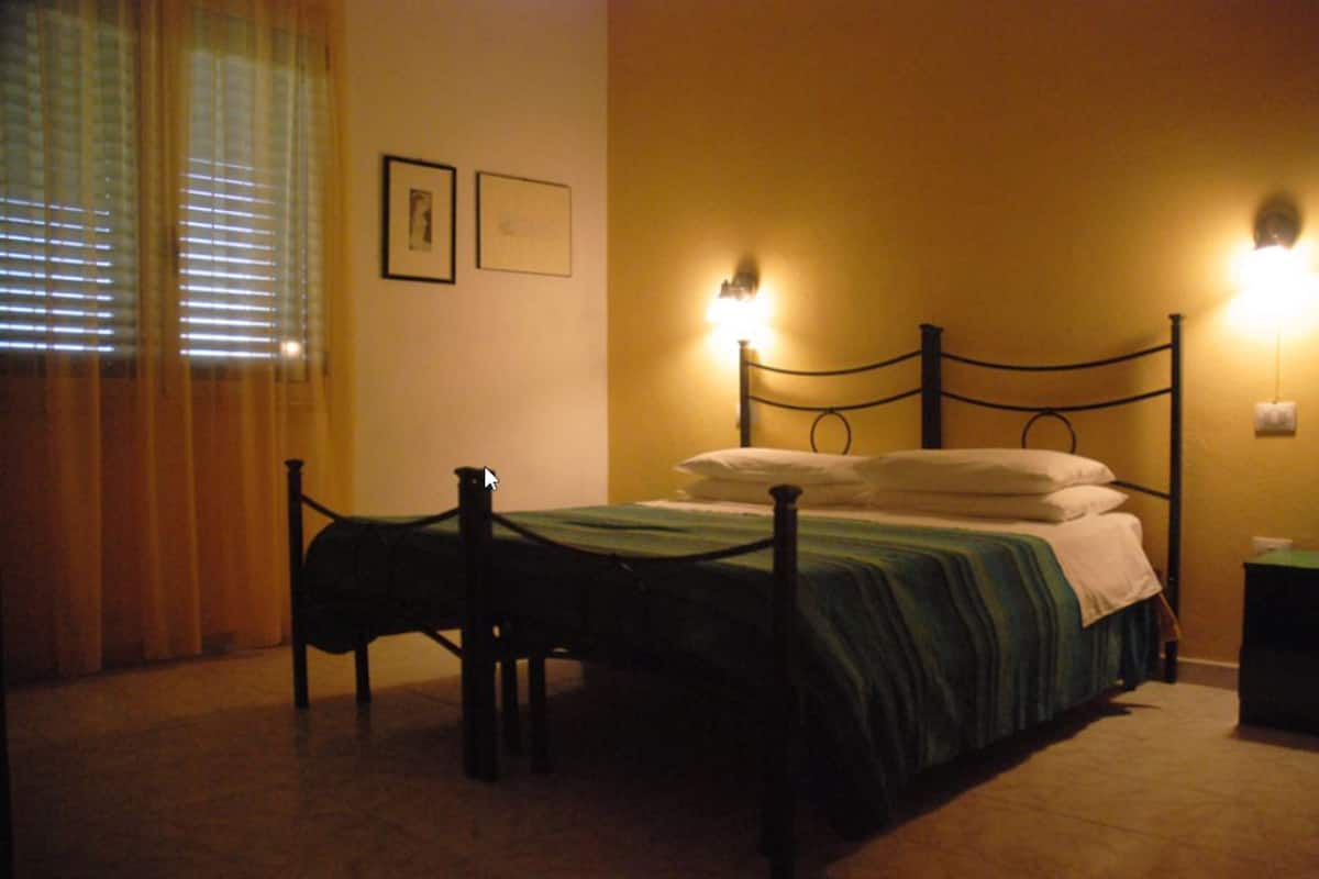 A dimly lit room with a bed, a chair, and two wall-mounted lamps.