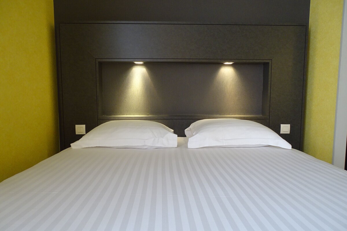 Une chambre d’hôtel avec un grand lit, deux oreillers et une tête de lit dotée d’un éclairage intégré.