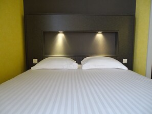 Une chambre d’hôtel avec un grand lit, deux oreillers et une tête de lit dotée d’un éclairage intégré.
