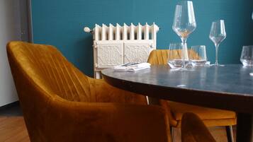 Un coin repas avec une table ronde, deux chaises de couleur moutarde et un radiateur blanc, le tout adossé à un mur de couleur turquoise.
