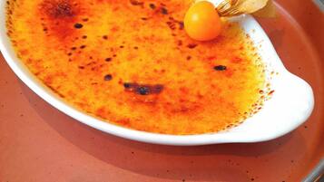 Un plat blanc nappé d’une sauce orange crémeuse, décoré d’une cerise et d’une feuille, le tout présenté sur une assiette rouge.