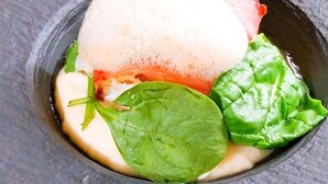 Un plat composé d’un élément blanc en forme de sphère, de feuilles vertes et d’une tranche de viande rouge, le tout présenté sur une assiette sombre.
