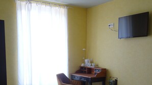 Une chambre d’hôtel avec deux lits, un bureau, une chaise, une télévision et une fenêtre avec des rideaux.