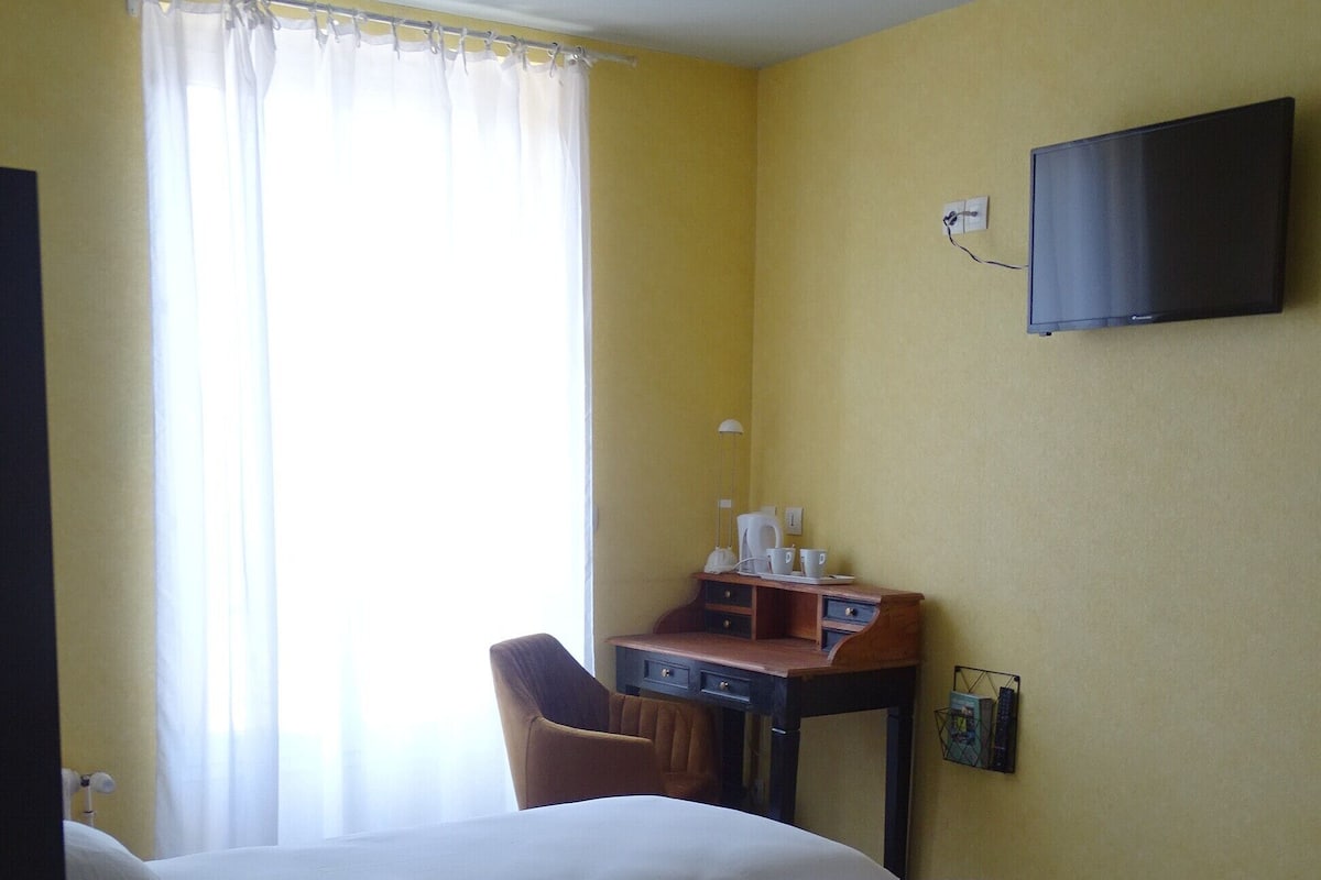 A hotel room with two beds, a desk, a chair, a television, and a window with curtains.