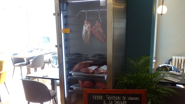 L'intérieur d'un restaurant, avec un présentoir à viande et un menu écrit à la craie.