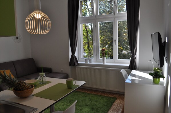 A modern living room with a sofa, a dining table with a pineapple, a hanging light fixture, and a view of trees through the window. - Studio Apartments City&style (Zagreb)