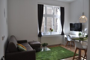 A modern living room with a sofa, a glass coffee table, a green rug, a TV, and a desk with a chair. - Studio Apartments City&style (Zagreb)