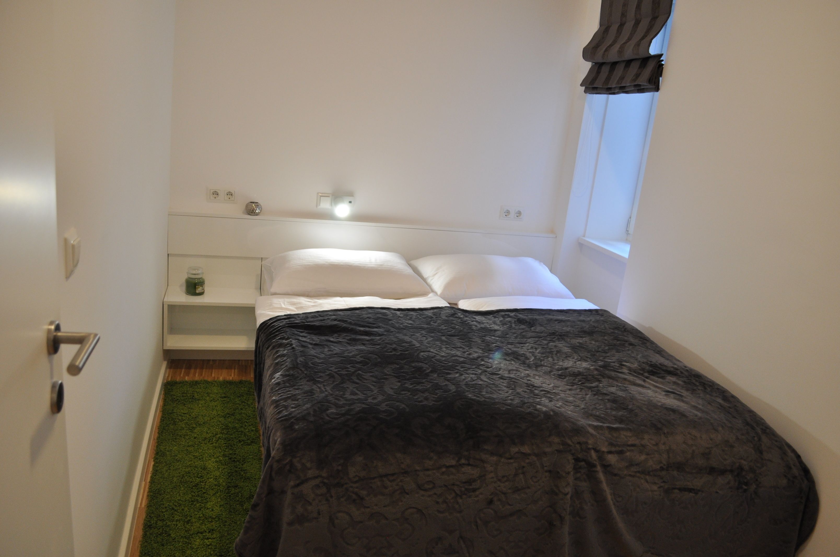A small, neatly arranged bedroom with a bed, bedside table, and a nightstand.