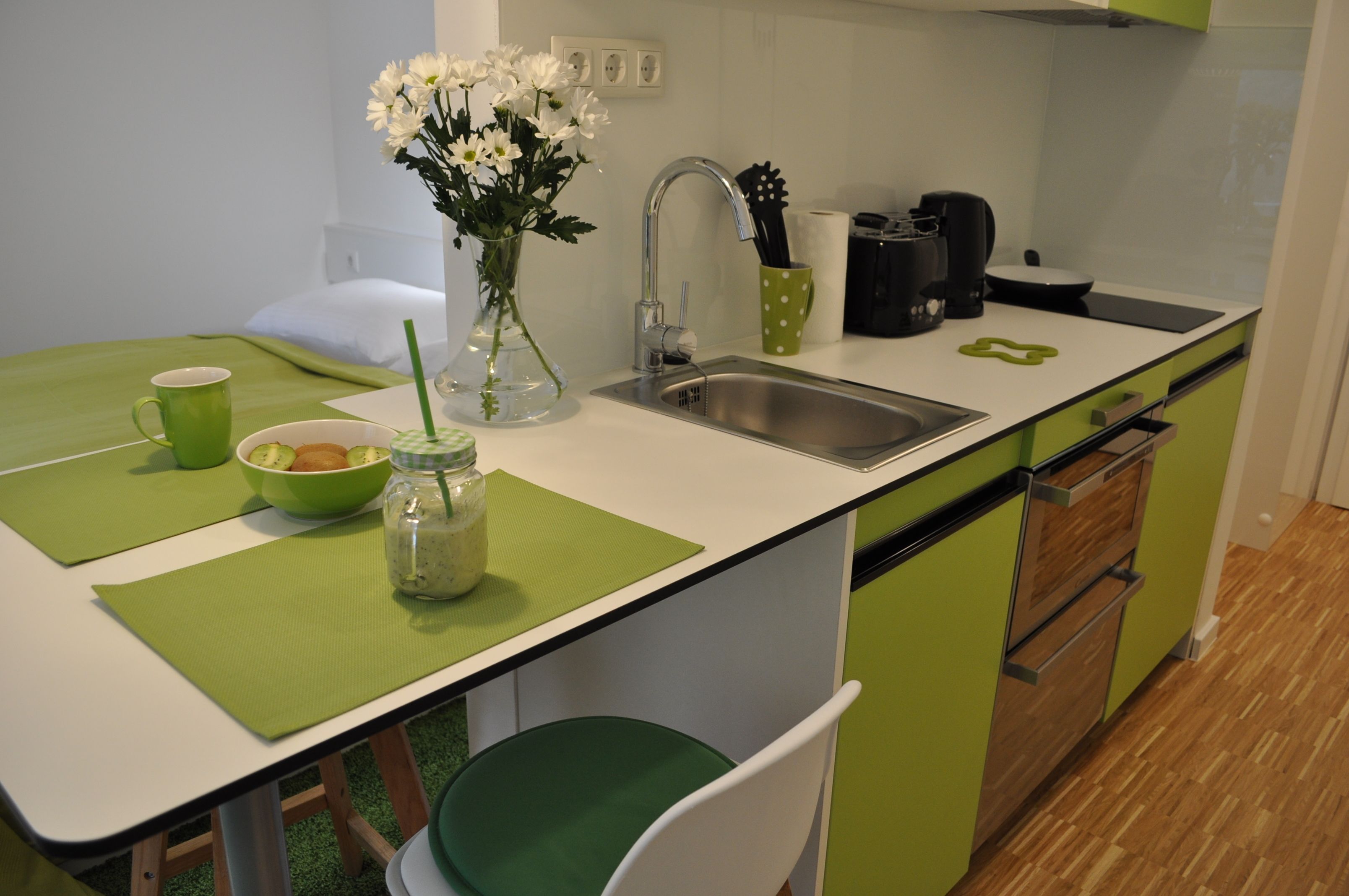 Une cuisine avec un évier, un plan de travail vert et blanc, et une chaise.