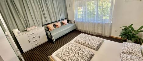 Une chambre à coucher comprenant un lit, une table de chevet, une commode, une fenêtre avec des rideaux et une plante en pot.