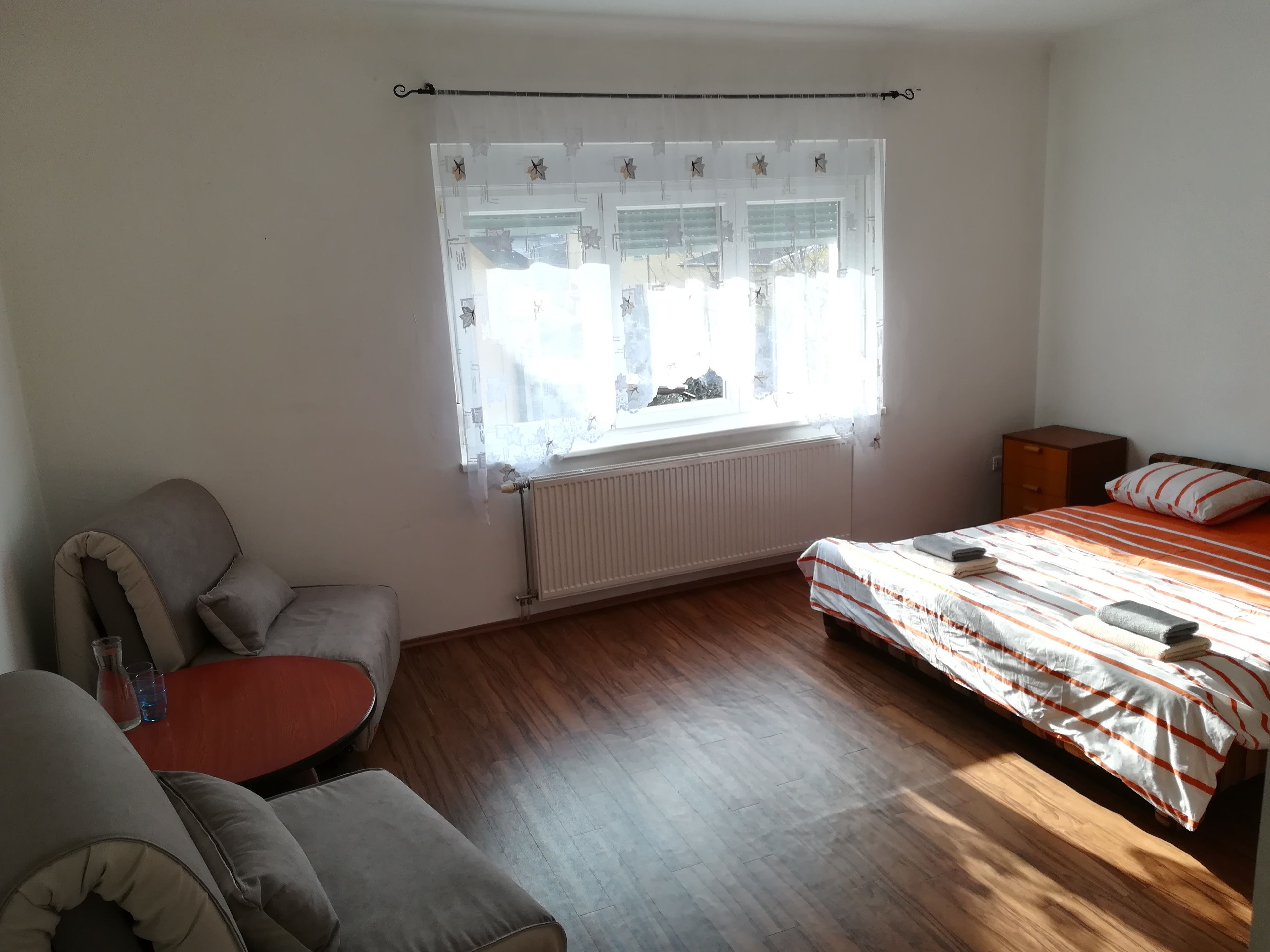 A bedroom with a bed, a chair, a small table, and a window with curtains.