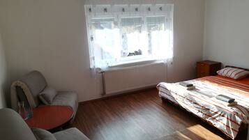 A bedroom with a bed, a chair, a small table, and a window with curtains.