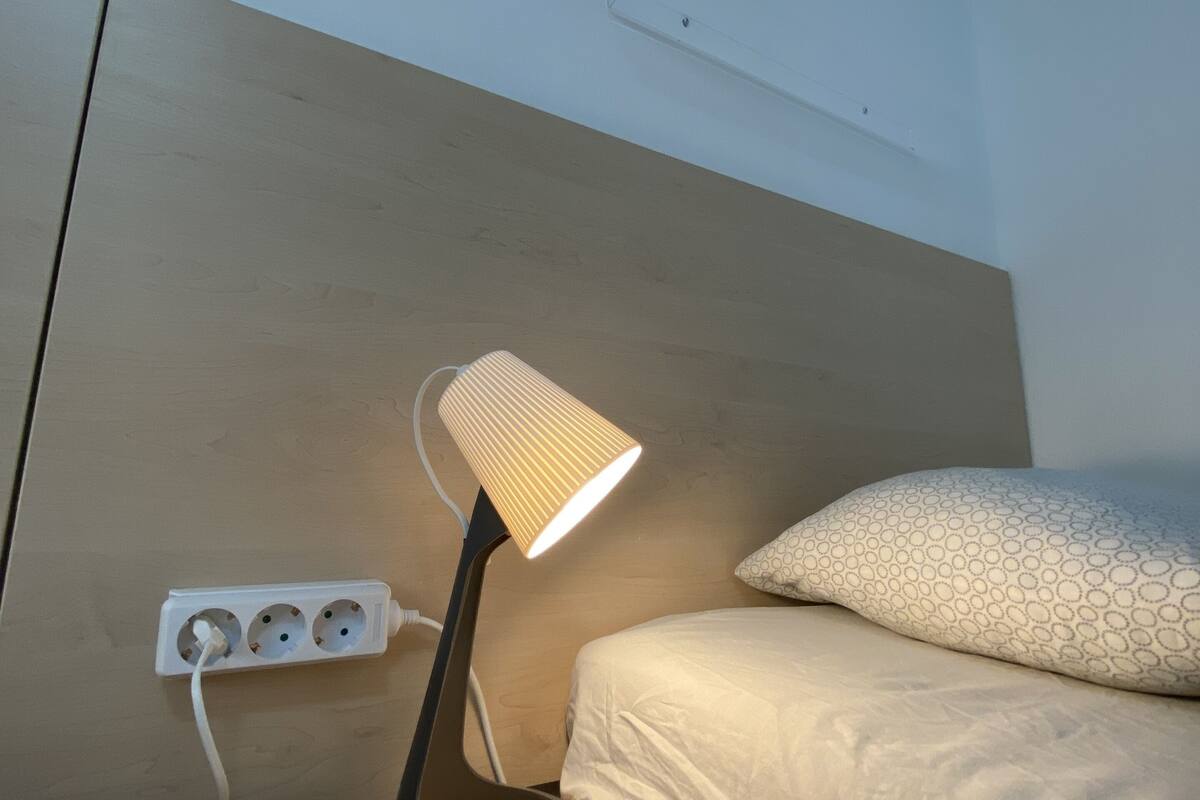 Une table de chevet avec une lampe, une multiprise et une prise de courant murale.