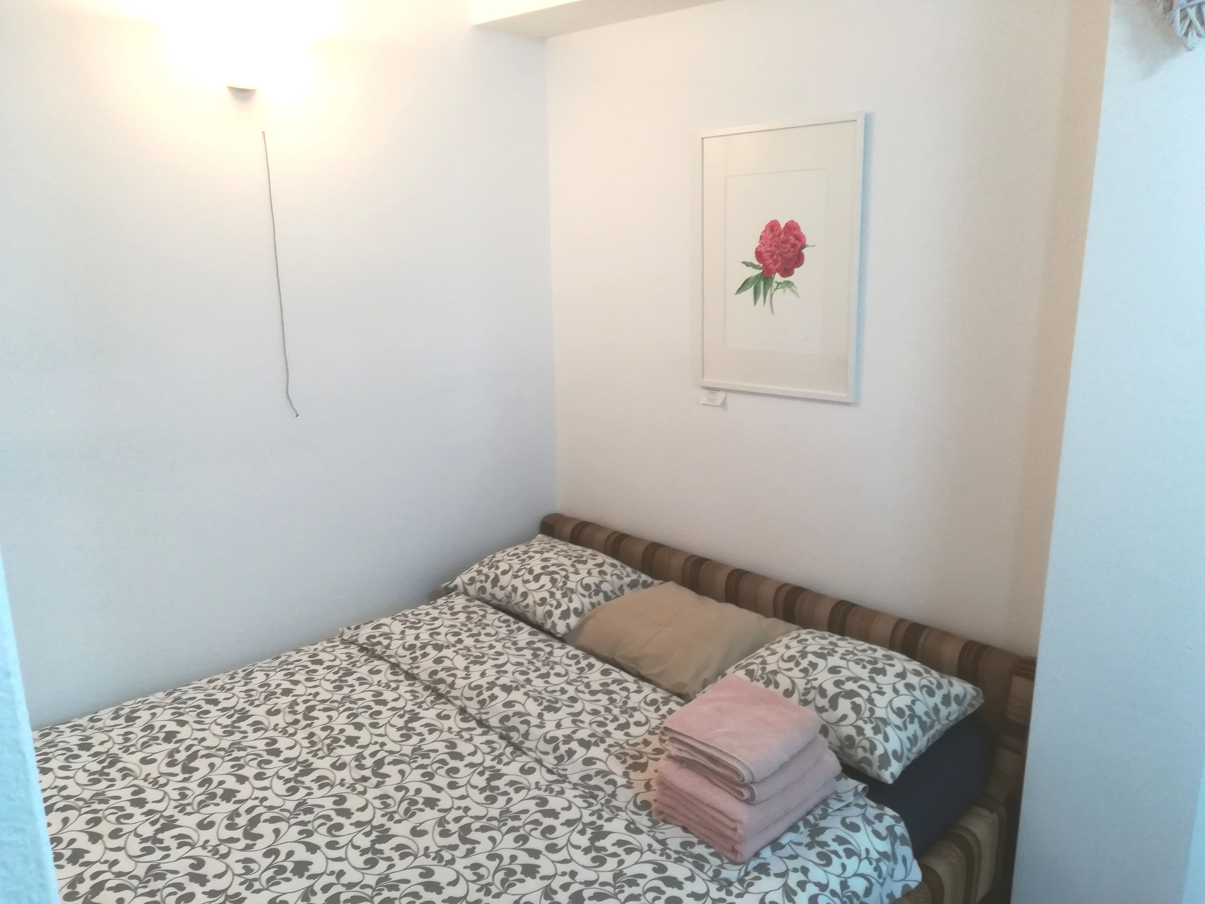 A small, neatly arranged bedroom with a patterned bedspread, a single pillow, and a stack of folded towels.