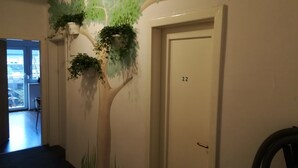 Un pasillo con un mural de un árbol, una puerta con la etiqueta '22' y una silla.