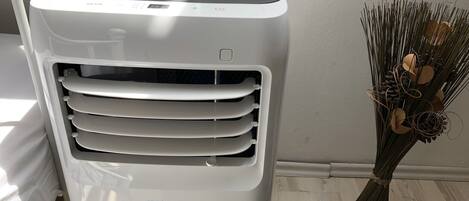 Un climatiseur blanc doté d’un écran numérique, portant l’inscription « PRO KLIMA », se trouve dans une pièce dont le sol est en bois et qui est agrémentée d’une plante décorative.