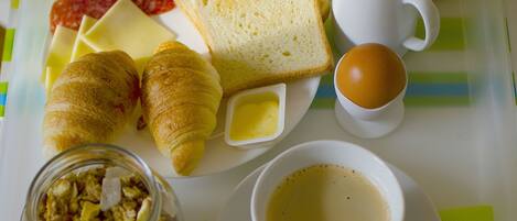 A breakfast tray with croissants, toast, jam, butter, a cup of coffee, a small jar of cereal, and a container of yogurt.