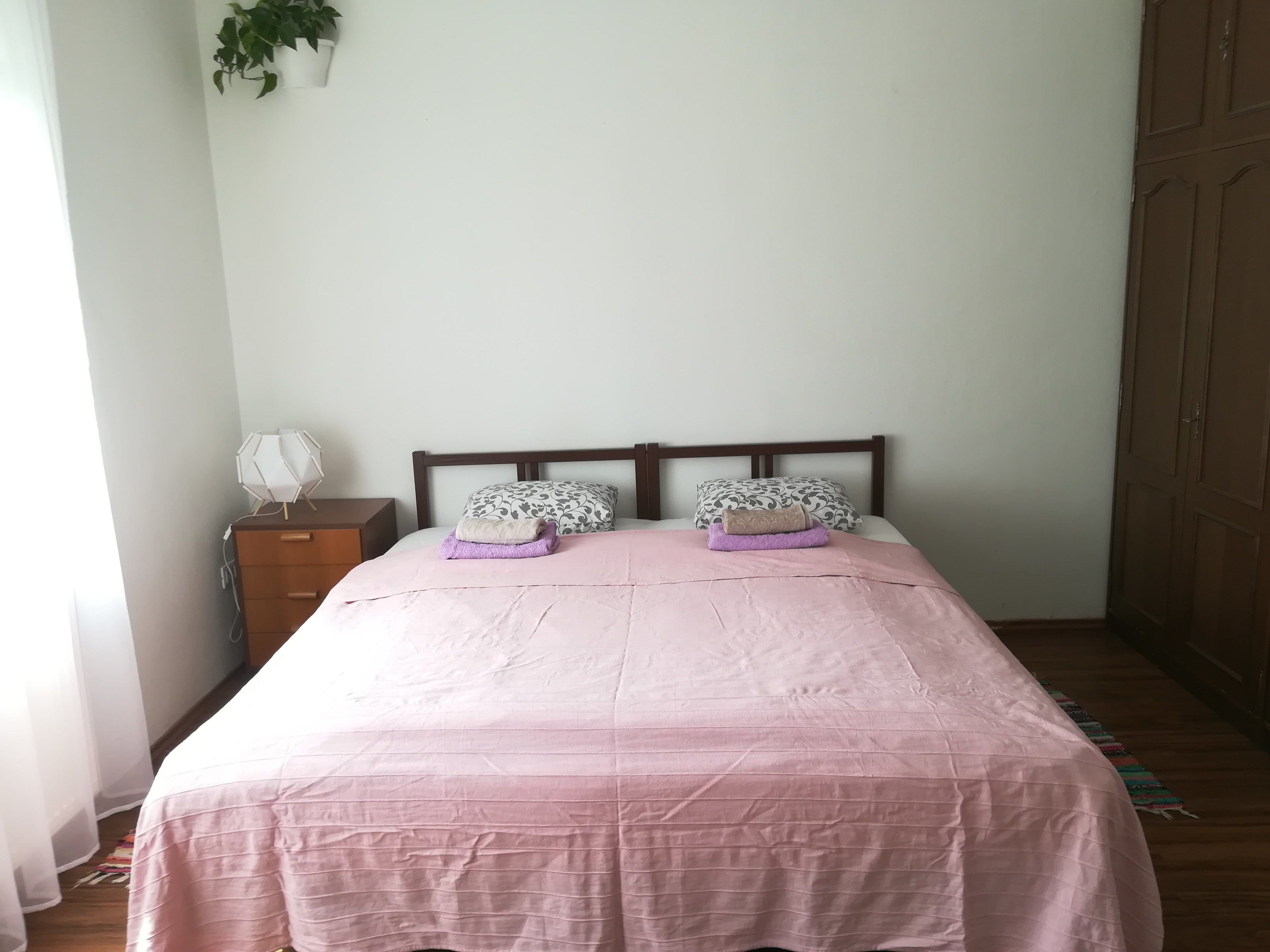 Una camera da letto con un letto, due cuscini, un comodino, una lampada, una cassettiera e un armadio.