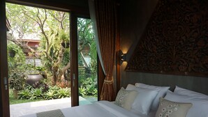 A bedroom with a large bed, a view of a garden, and a decorative wall. - Baansuwanburi (San Sai)