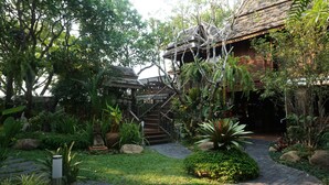 A traditional wooden house with a staircase leading to a wooden deck. - Baansuwanburi (San Sai)