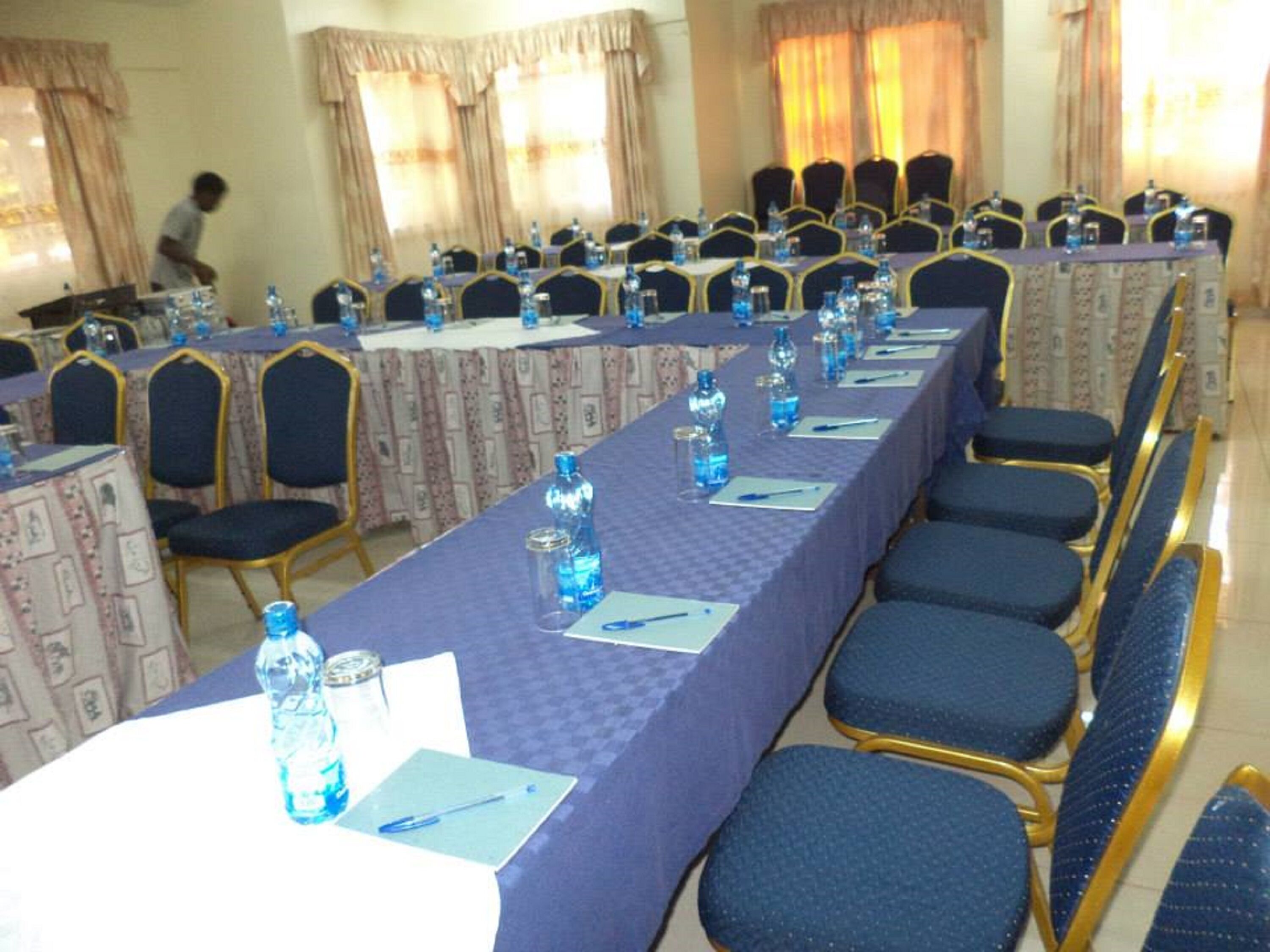 A conference room with rows of tables and chairs, water bottles, and name cards on each table.