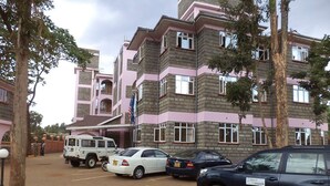 Un edificio de varios pisos con fachada rosa y gris, coches aparcados y una bandera.