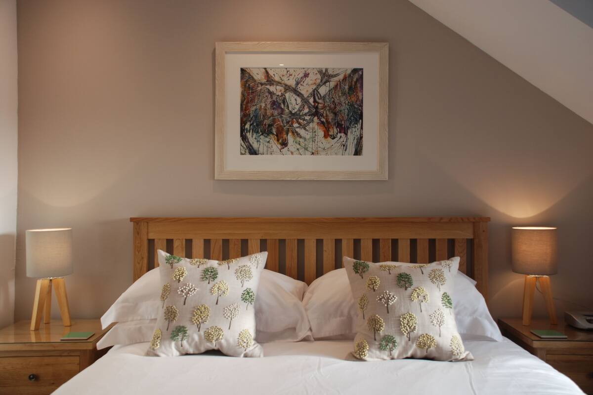 A bedroom with a wooden headboard, two bedside lamps, and a framed abstract painting on the wall.