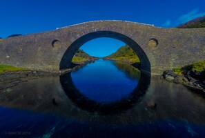 Un puente de piedra en arco sobre un río tranquilo, con cielo azul despejado arriba.