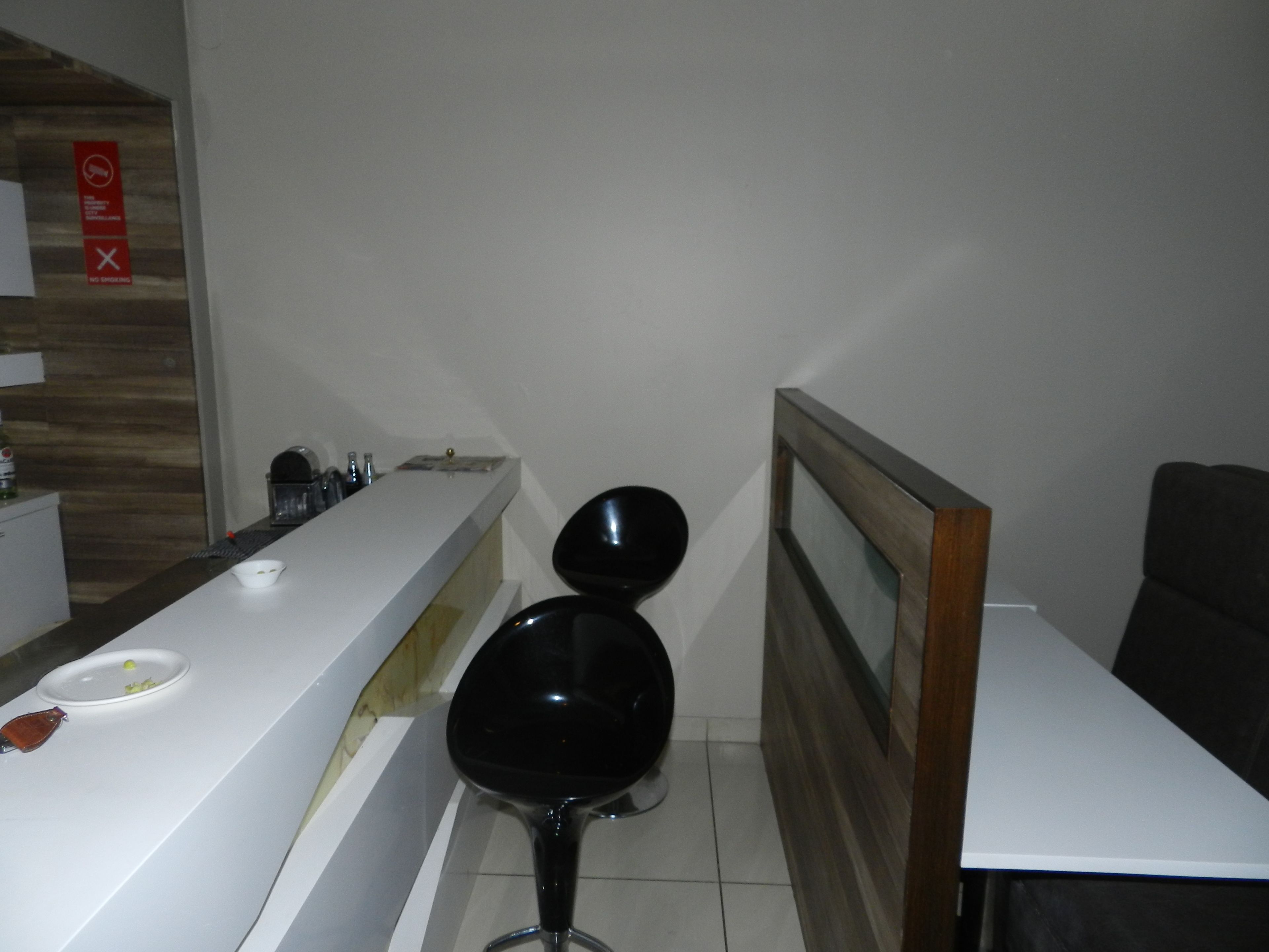 A modern hotel room with a white reception desk, a black chair, and a wooden-framed mirror.