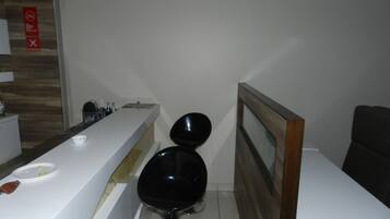 A modern hotel room with a white reception desk, a black chair, and a wooden-framed mirror.