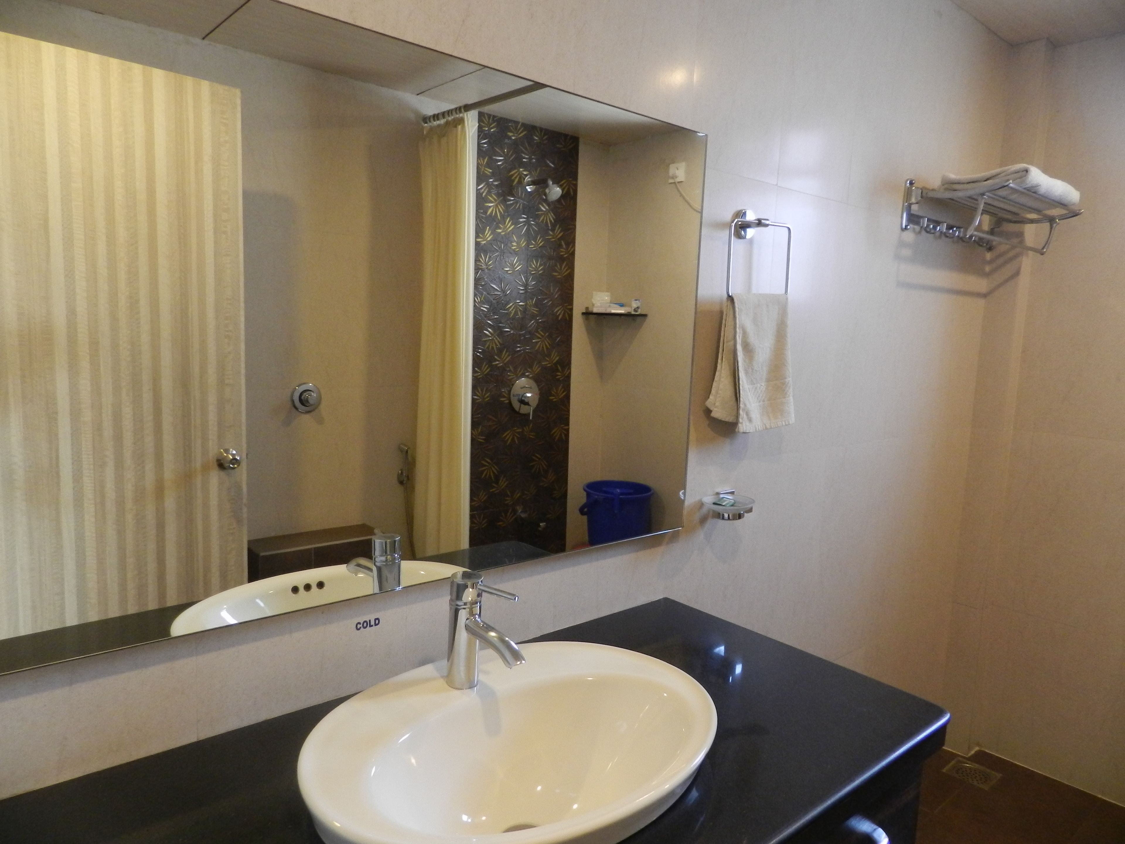 Un baño con un lavamanos blanco, un espejo, un perchero para toallas y una zona de ducha.