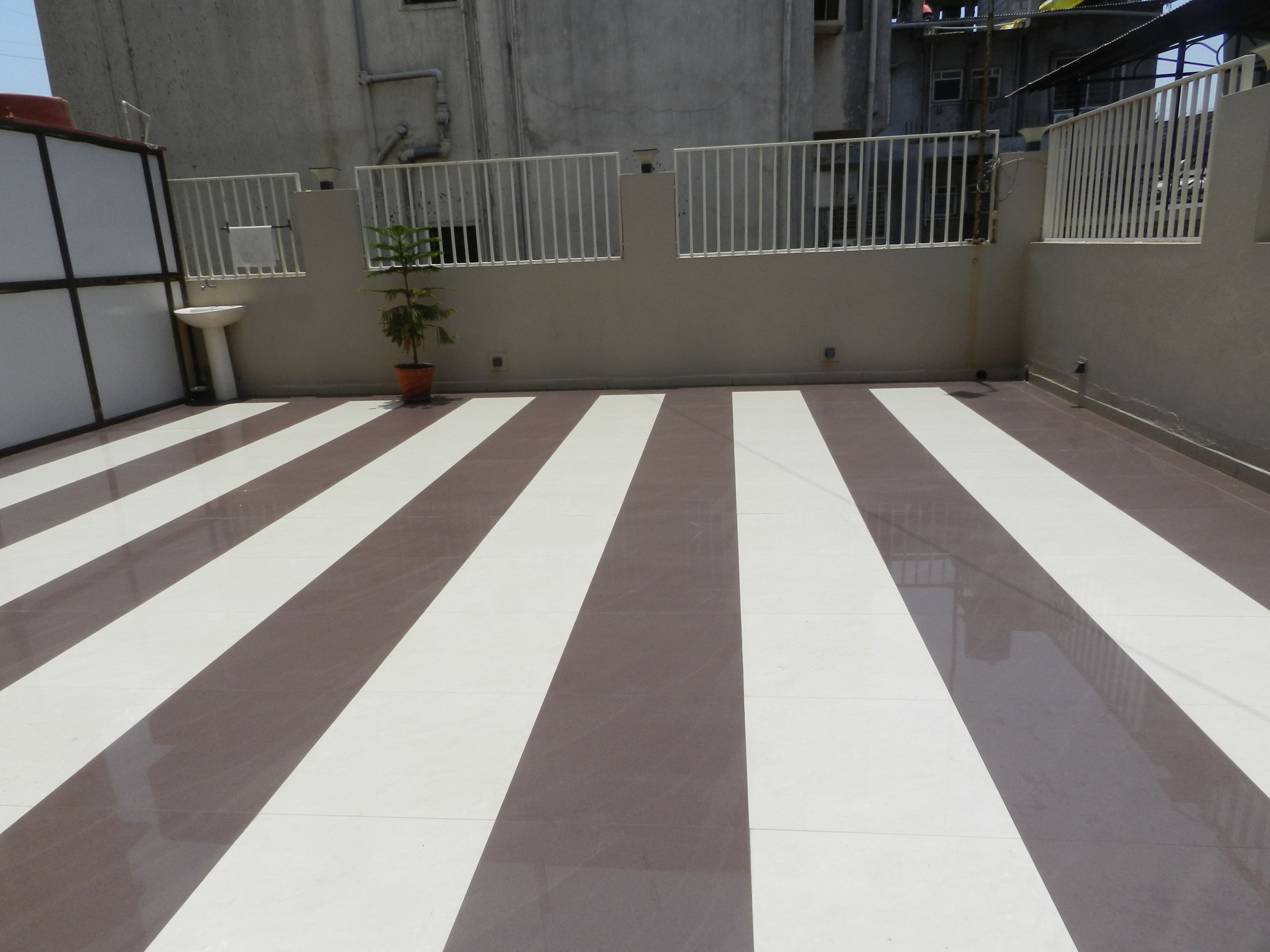 A rooftop terrace with striped flooring, a potted plant, and a white railing.