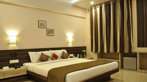 Ein Hotelzimmer mit einem großen Bett, Nachttischen, einem Schreibtisch, einer Lampe, einem kleinen Kühlschrank und einem roten Teppich mit Muster.
