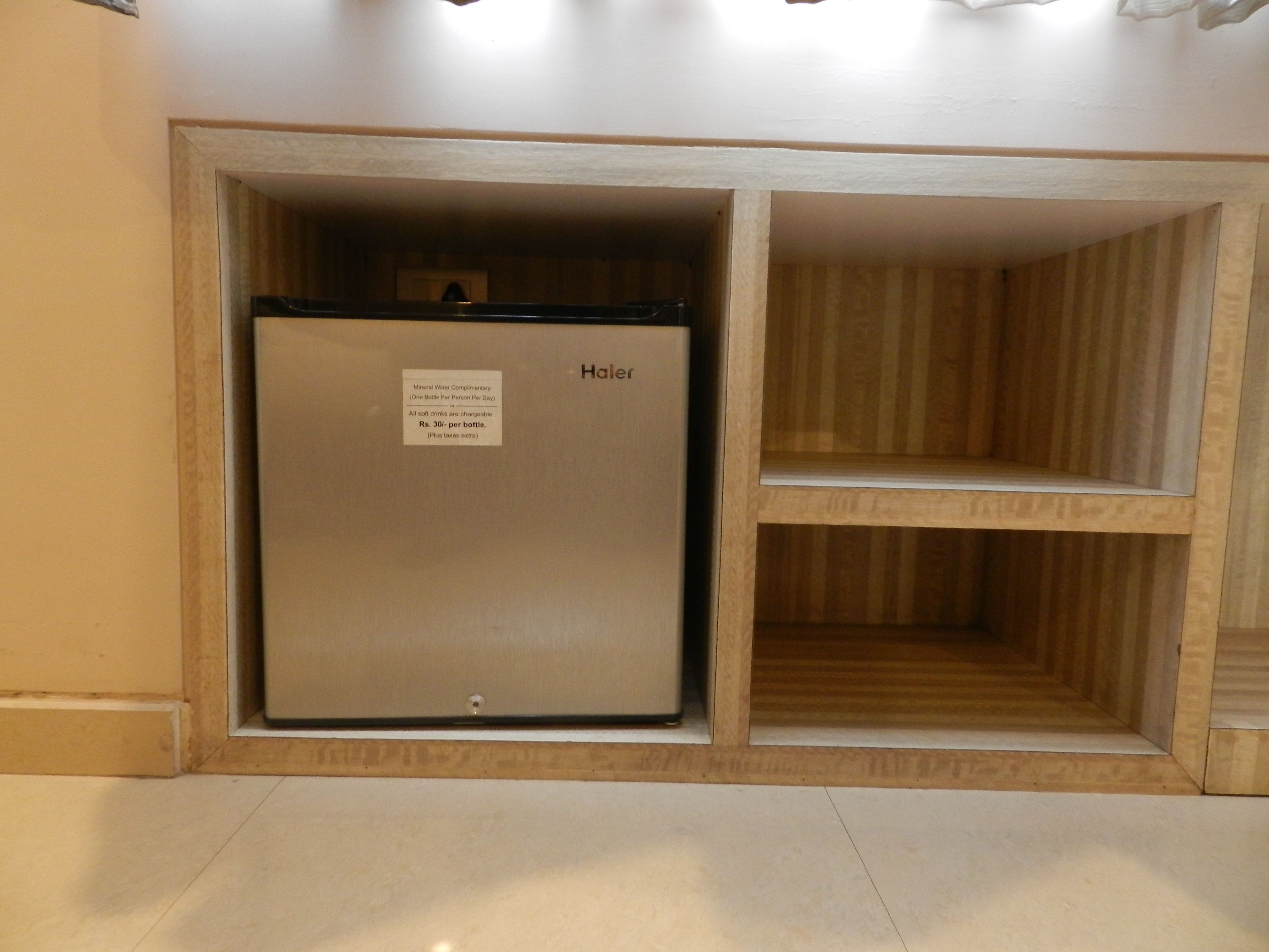 A compact refrigerator with a label indicating it is a mineral water complimentary refrigerator, priced at Rs. 30 per bottle plus taxes.