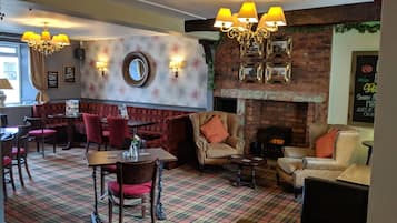 Interior de restaurante con piso a cuadros, asientos tapizados en rojo y beige, chimenea de ladrillo y lámparas de pared.