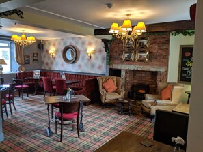 A restaurant interior with checkered flooring, red and beige upholstered seating, a brick fireplace, and wall-mounted lamps. - The Queens Head (Durham)