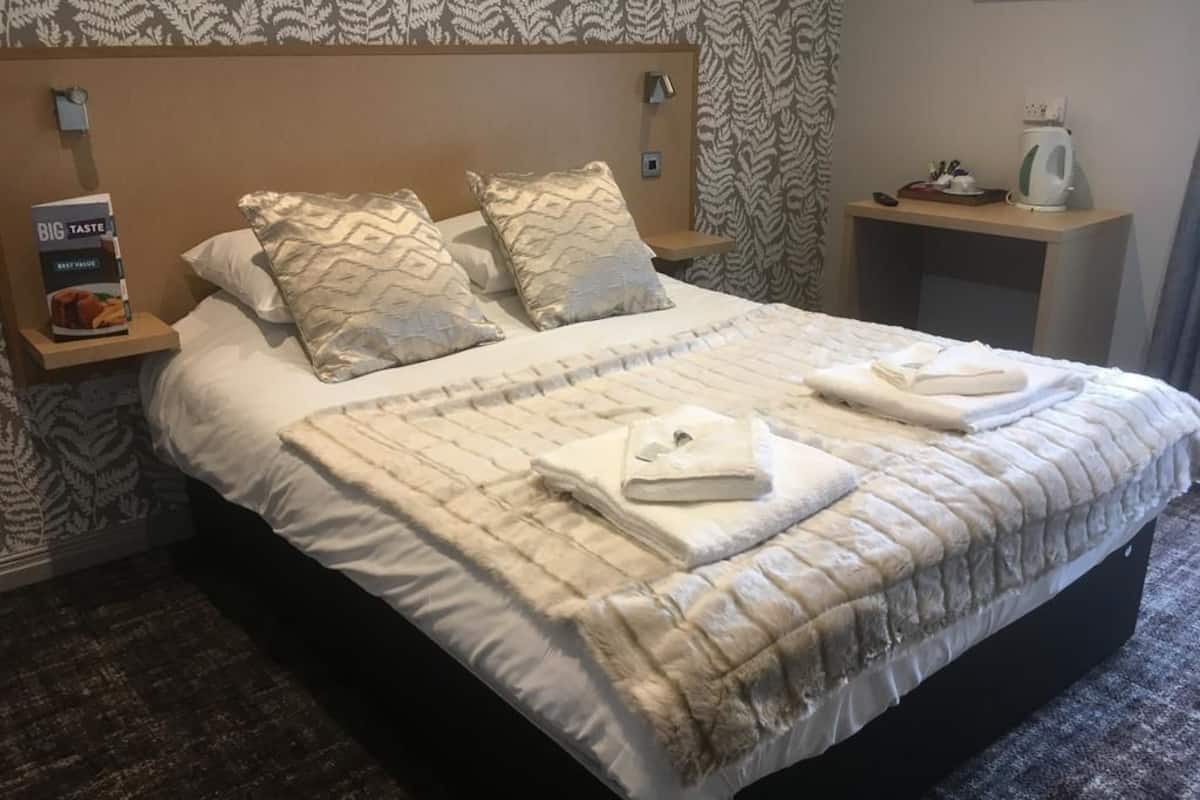 Una cama bien hecha con un cabecero estampado, dos almohadas y dos toallas dobladas sobre la cama.