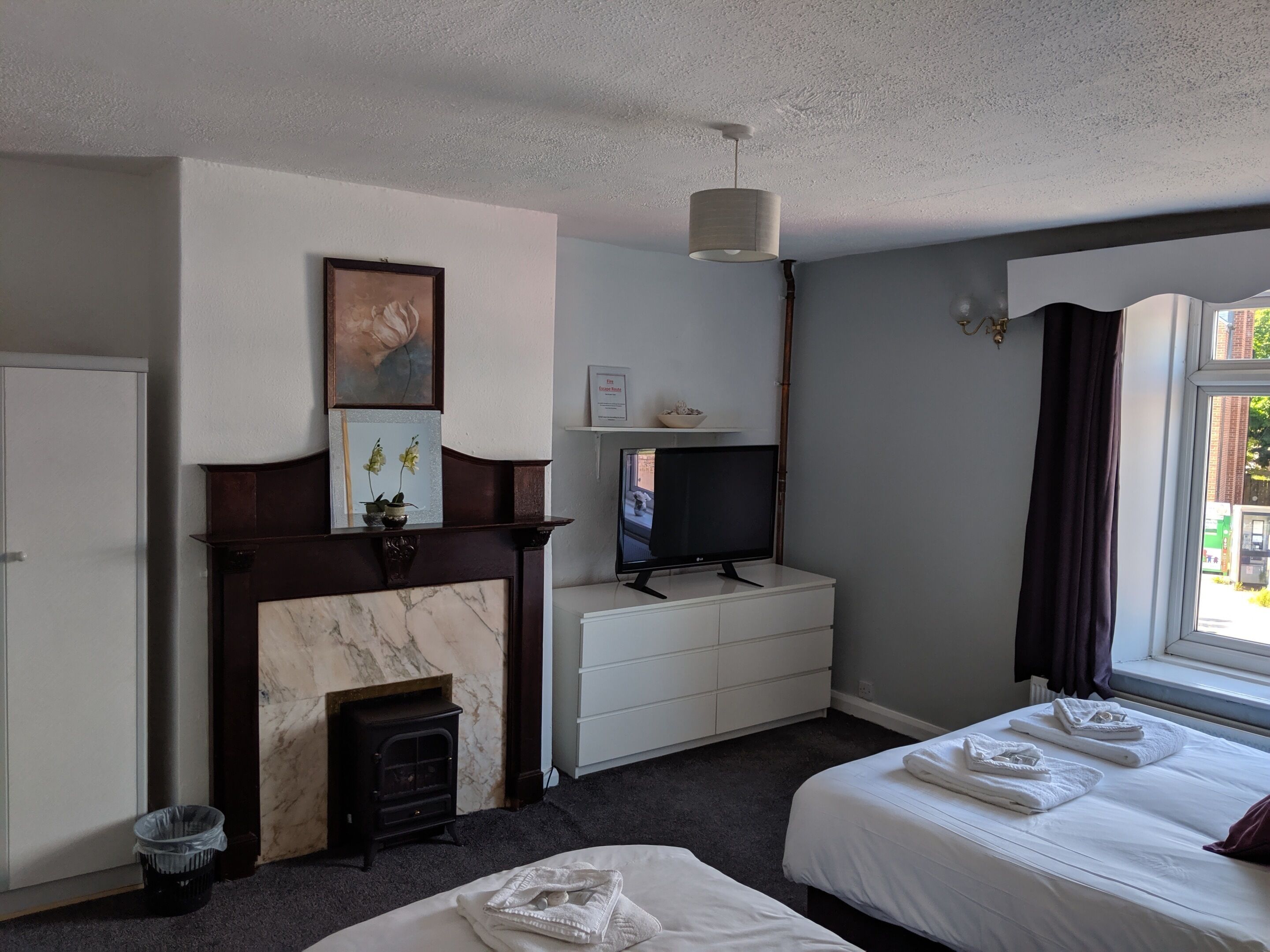 Une chambre d’hôtel avec une cheminée, une télévision, un lit avec des serviettes et une fenêtre avec des rideaux.