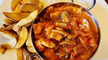 Een bord met een kom curry en frietjes, een ketchupfles en een glas water op een houten tafel.